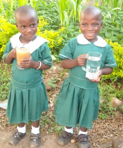 Twins Lydia and Barbara are holding two glasses of water. The first is the water the used to drink, dirty and filled with disease. The second the clean water of the Jesse well built in their village of Busolo, Uganda. 