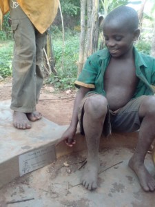 This boy is sitting on the concrete of the borehole and pointing at the plaque .